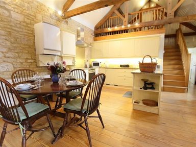 A kitchen with wooden dining table and chairs stone walls and wooden beams at The Granary in Bourton-On-The-Water