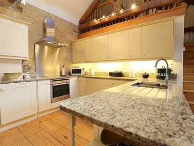 A kitchen with stone walls wooden floors cream cabinets and granite countertops at The Granary in Bourton-On-The-Water
