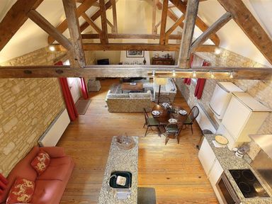An open living space with exposed wooden beams stone walls wooden floor a kitchen area with granite countertops a round dining table set for four and two sofas at The Granary in Bourton-On-The-Water