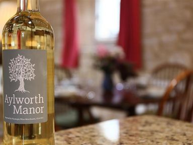 A bottle of Aylworth Manor white wine on a kitchen counter with wooden chairs and a dining table in the background at The Granary in Bourton-On-The-Water