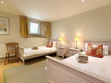 A bedroom with two single beds bedside tables with lamps and a wooden chair at The Granary in Bourton-On-The-Water