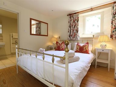 A bedroom with a metal bed frame with pillows and towels on the bed bedside tables with lamps and a window with floral curtains at The Granary in Bourton-On-The-Water
