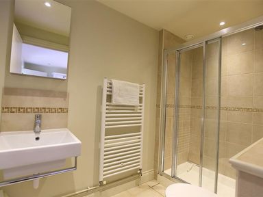 A bathroom with a wall-mounted sink a heated towel rail and a shower with glass sliding doors at The Granary in Bourton-On-The-Water