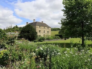A house with a garden full of flowers and a tree in a rural setting at The Granary in Bourton-On-The-Water