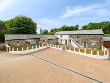 An exterior view of a stone and white building with a fenced courtyard and paved driveway at The Granary in Davidstow near Camelford