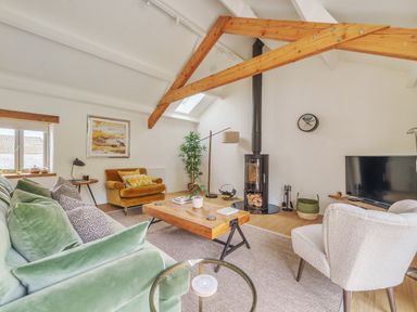 A living room with green sofa yellow armchair and white chair with wooden beams at The Granary in Davidstow near Camelford