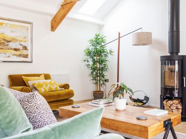 A living room with a wooden coffee table plant a yellow armchair and a black wood stove at The Granary in Davidstow near Camelford