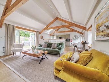 An open living room and kitchen area with wooden beams two sofas a coffee table and a dining table at The Granary in Davidstow near Camelford