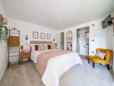 A bedroom with a double bed a yellow chair a ladder with blankets an en suite bathroom and a wall-mounted tv at The Granary in Davidstow near Camelford