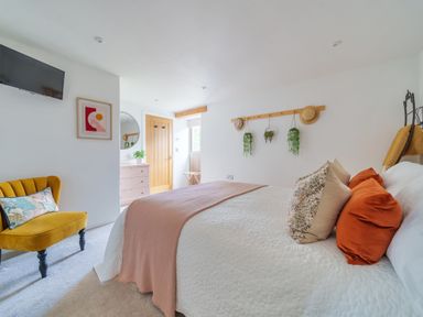 A bedroom with a bed a yellow chair a dresser and plants hanging on a wall at The Granary in Davidstow near Camelford