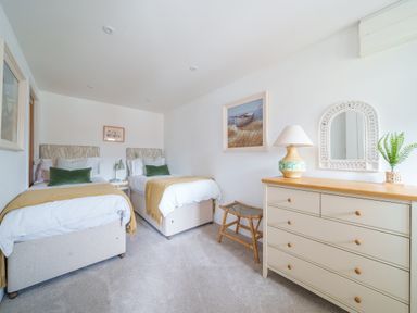 A bedroom with two single beds a dresser with lamp and mirror and a small bench at The Granary in Davidstow near Camelford