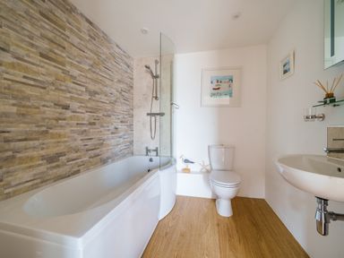 A bathroom with a bathtub shower toilet sink wooden floor and wall art at The Granary in Davidstow near Camelford