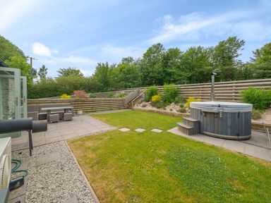 A garden with a wooden hot tub, patio table with chairs, gravel path, and raised planting beds at The Granary in Davidstow near Camelford
