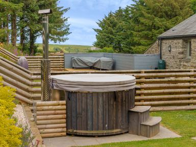An outdoor hot tub with a cover and wooden steps in a garden next to a stone building at The Granary in Davidstow near Camelford