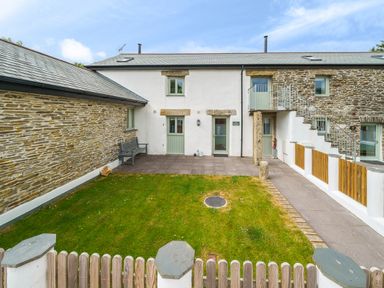 A courtyard with green grass and stone patio surrounded by stone and white walls at The Granary in Davidstow near Camelford