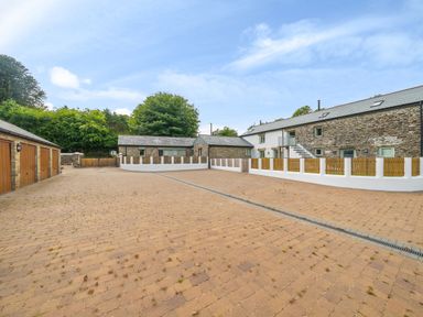 A paved courtyard with garages on the left and stone buildings with wooden fences on the right at The Granary in Davidstow near Camelford