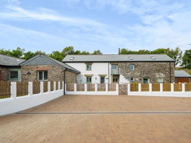 A stone and white painted house with a paved driveway and wooden fencing at The Granary in Davidstow near Camelford