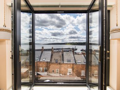 A view through open glass doors showing rooftops and a harbor with boats and a lighthouse visible at Casa Formentera in Scarborough