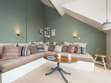 A living area with an L shaped cushioned bench with striped pillows and a wooden oval coffee table with two mugs and a magazine at Casa Formentera in Scarborough