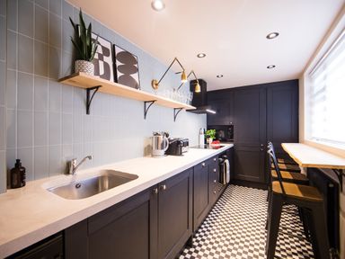 A kitchen with black cabinets a white countertop a black and white checkered floor and bar stools at Casa Formentera in Scarborough