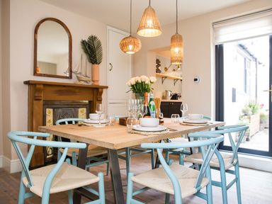 A dining area with a wooden table set with dishes and glasses and surrounded by blue chairs near a fireplace at Casa Formentera Scarborough