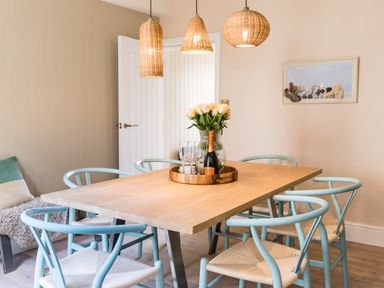 A dining room with a wooden table surrounded by light blue chairs a vase with flowers and a bottle on the table at Casa Formentera in Scarborough