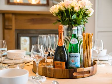A dining table with a wooden tray holding a bottle of prosecco a bottle of san pellegrino breadsticks and wine glasses at Casa Formentera Scarborough