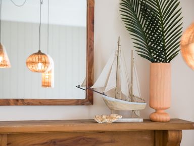 A wooden mantel with a model sailboat, a shell, and a tall vase with green leaves next to a wooden framed mirror at Casa Formentera in Scarborough