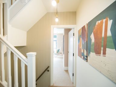 A hallway with stairs on the left and abstract paintings on the wall at Casa Formentera in Scarborough