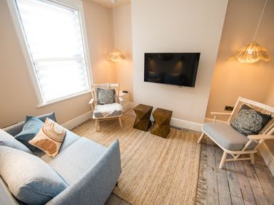A living room with a blue sofa two chairs two pendant lights a wall mounted television and a large woven rug at Casa Formentera in Scarborough