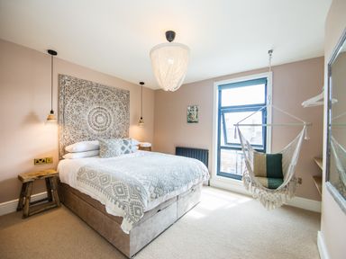 A bedroom with a bed a wooden stool pendant lights a hanging chair and a window at Casa Formentera in Scarborough