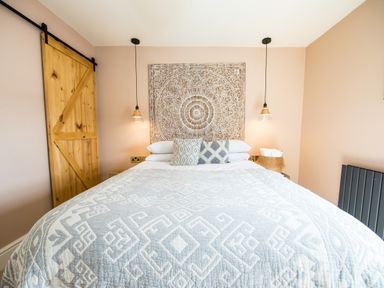 A bedroom with a large bed with patterned bedding three pillows two hanging pendant lights a wooden sliding door and a carved wall decoration at Casa Formentera in Scarborough