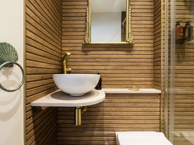 A bathroom with a white round sink gold faucet wooden slat walls and a gold framed mirror at Casa Formentera in Scarborough