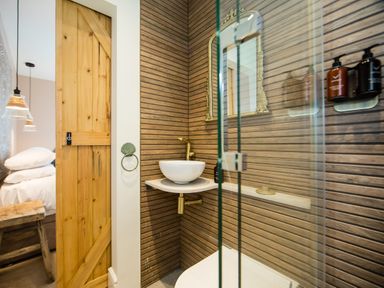 A bathroom with a wooden sliding door a white vessel sink a gold faucet a mirror and wall-mounted soap dispensers at Casa Formentera in Scarborough