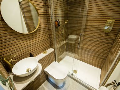 A bathroom with a round mirror a white sink a toilet and a shower with glass doors and brown wooden paneling at Casa Formentera in Scarborough