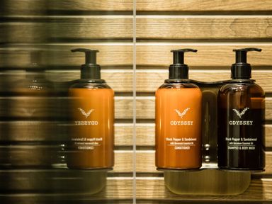 Two pump bottles of Odyssey shampoo body wash and conditioner mounted on a wall with horizontal wooden panels at Casa Formentera in Scarborough