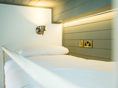 A single bed with white bedding against a wall with a metal wall light and electrical outlets at Casa Formentera Scarborough