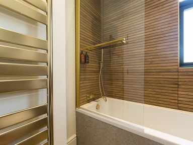 A bathroom with a bathtub shower combination and wood panel walls at Casa Formentera in Scarborough