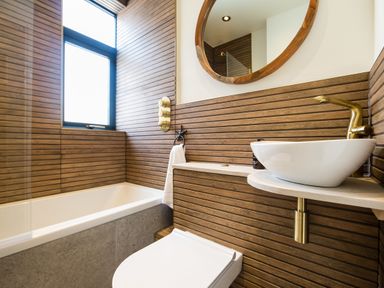 A bathroom with a bathtub toilet sink round mirror and wooden paneling at Casa Formentera in Scarborough