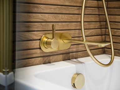 A close up of a gold bathtub faucet and handle with wood paneling behind at Casa Formentera in Scarborough