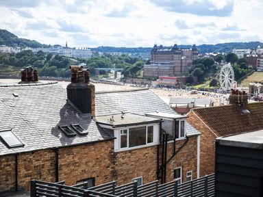 A view of rooftops with chimneys overlooking a beach and a ferris wheel in the background in Scarborough