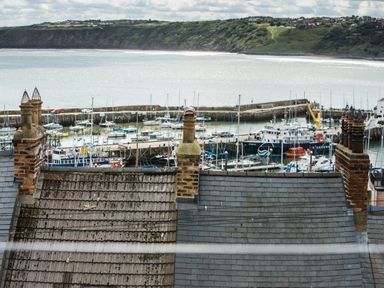 A harbor with boats docked behind rooftops and chimneys with a hill in the background at Casa Formentera in Scarborough
