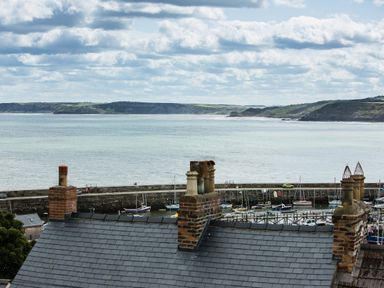 A coastal view with rooftops, chimneys, boats in a marina, a sea wall, water, and hills in the distance at Casa Formentera in Scarborough