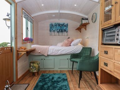 A small bedroom with a bed green chair wooden floor and wooden cabinets at Lottie's Hut in Okehampton