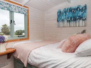 A small bedroom with a bed covered in blankets and pillows under a window with floral curtains at Lottie's Hut in Okehampton