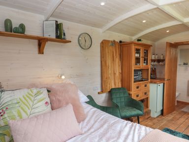 A bedroom with a bed pillows green chairs wooden cabinet and door at Lottie's Hut in Okehampton