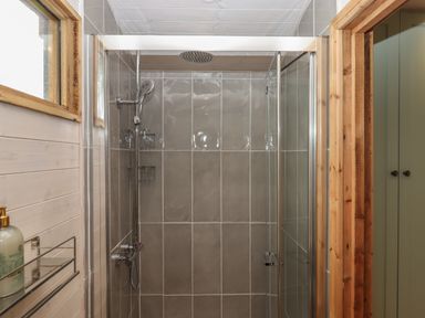A shower with gray tiles glass doors and a handheld showerhead at Lotties Hut in Okehampton