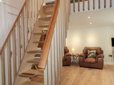 A wooden staircase next to a brown armchair with a patterned cushion and a side table with a lamp at The Studio at Dan y Garn Newport Pembrokeshire