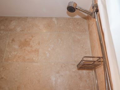 A shower area with beige tiled walls and a chrome showerhead and soap holder at The Studio at Dan y Garn in Newport Pembrokeshire