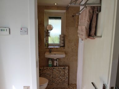 A small bathroom with a wall-mounted sink a toilet a frosted window and a towel rack with towels at The Studio at Dan y Garn in Newport Pembrokeshire